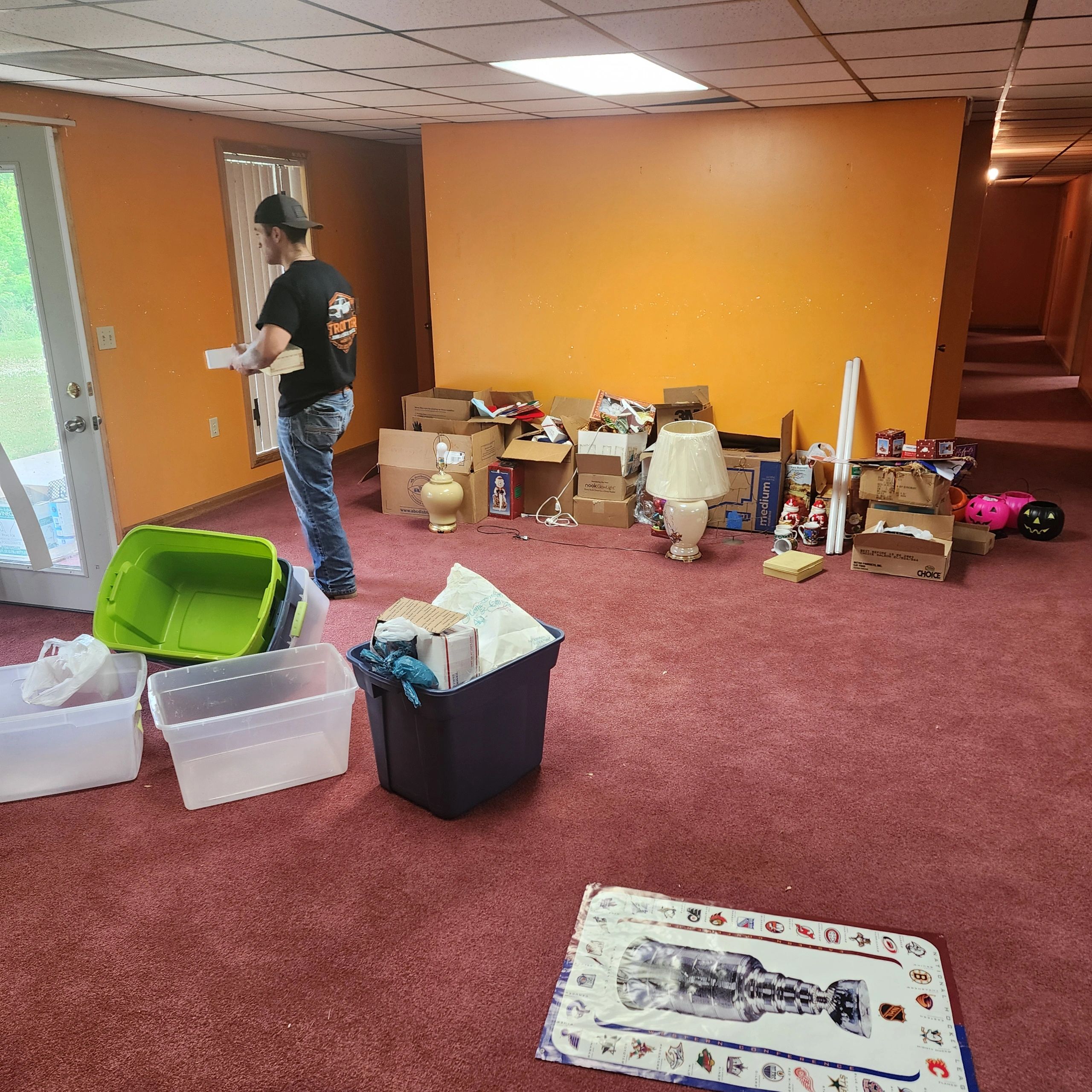 Man organizing boxes in a cluttered room with orange walls.