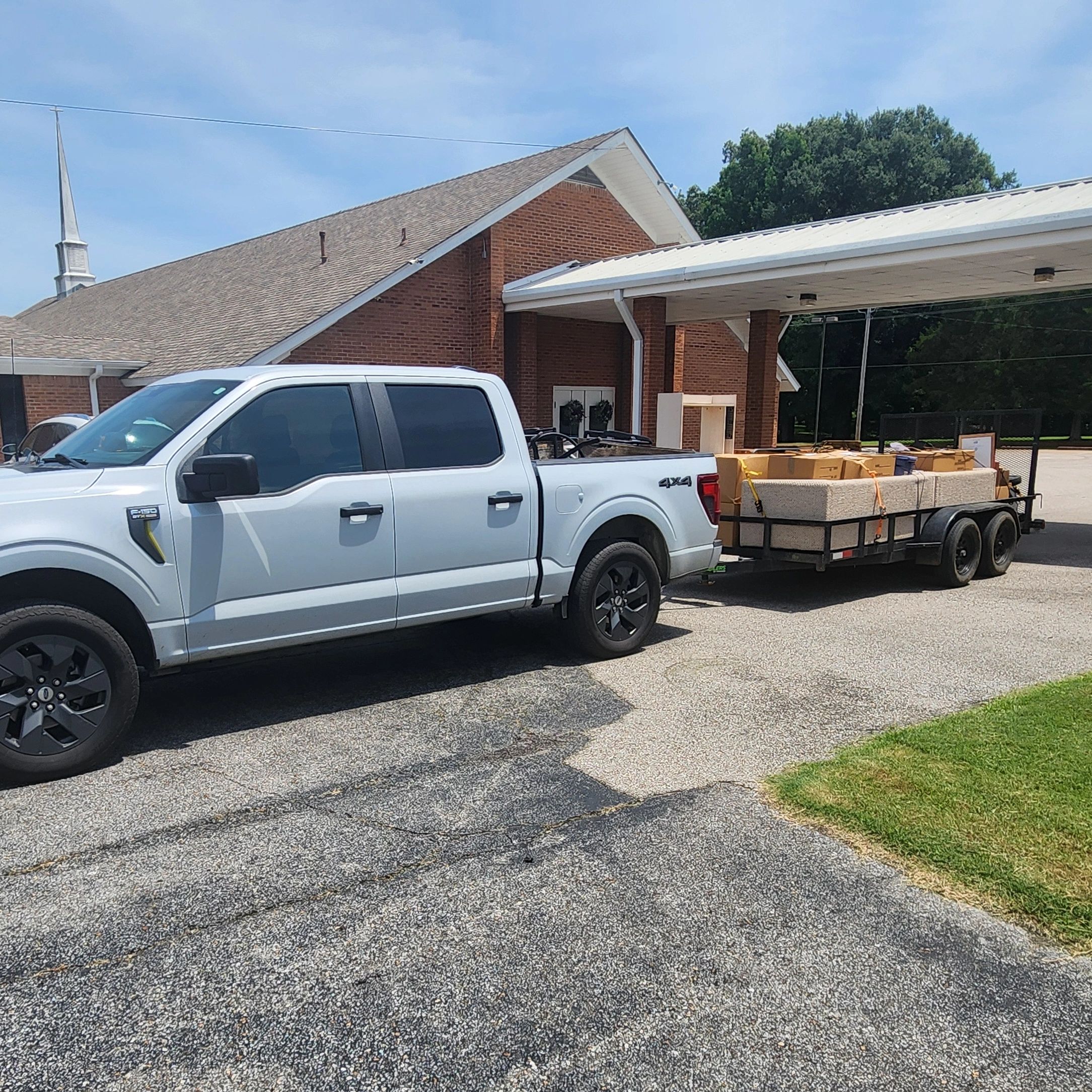 White pickup truck with a trailer full of boxes outside a church.