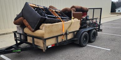 A trailer loaded with old couches and furniture secured by straps.