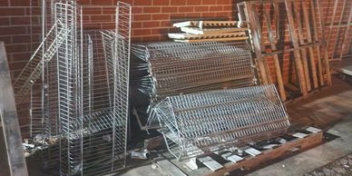 Stacked metal racks and wooden pallets outside against a brick wall.