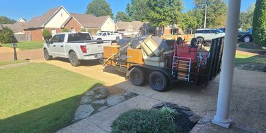 A white pickup truck towing a trailer loaded with furniture and bags.