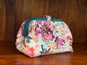 Floral fabric pouch with a teal zipper on wooden surface.