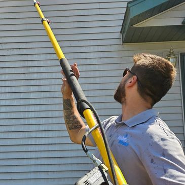 Man using a long pole tool to clean or repair the side of a house.