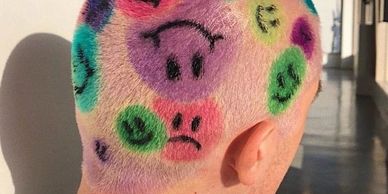 Head shaved and painted with colorful frowny and smiley faces.