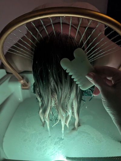 Person washing hair with a scalp massager in a basin of water.