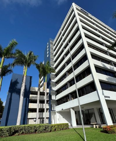 Modern white office building with palm trees and clear blue sky.