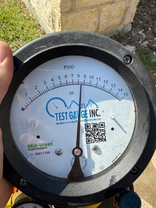 Close-up of a test gauge measuring pressure with a stone wall background.