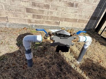 Outdoor water meter with blue valve handles and white PVC piping.