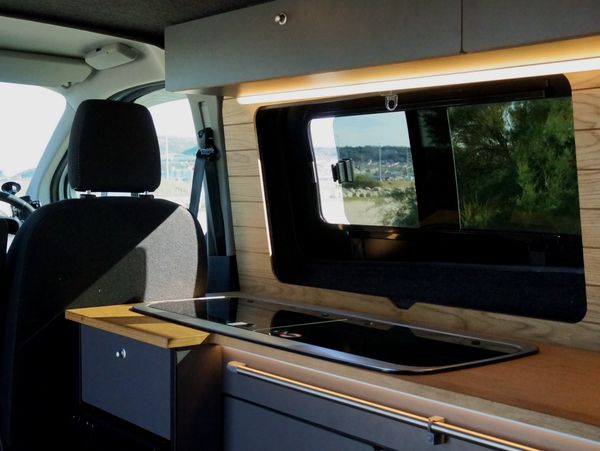 Modern camper van kitchen with stove and window overlooking nature.