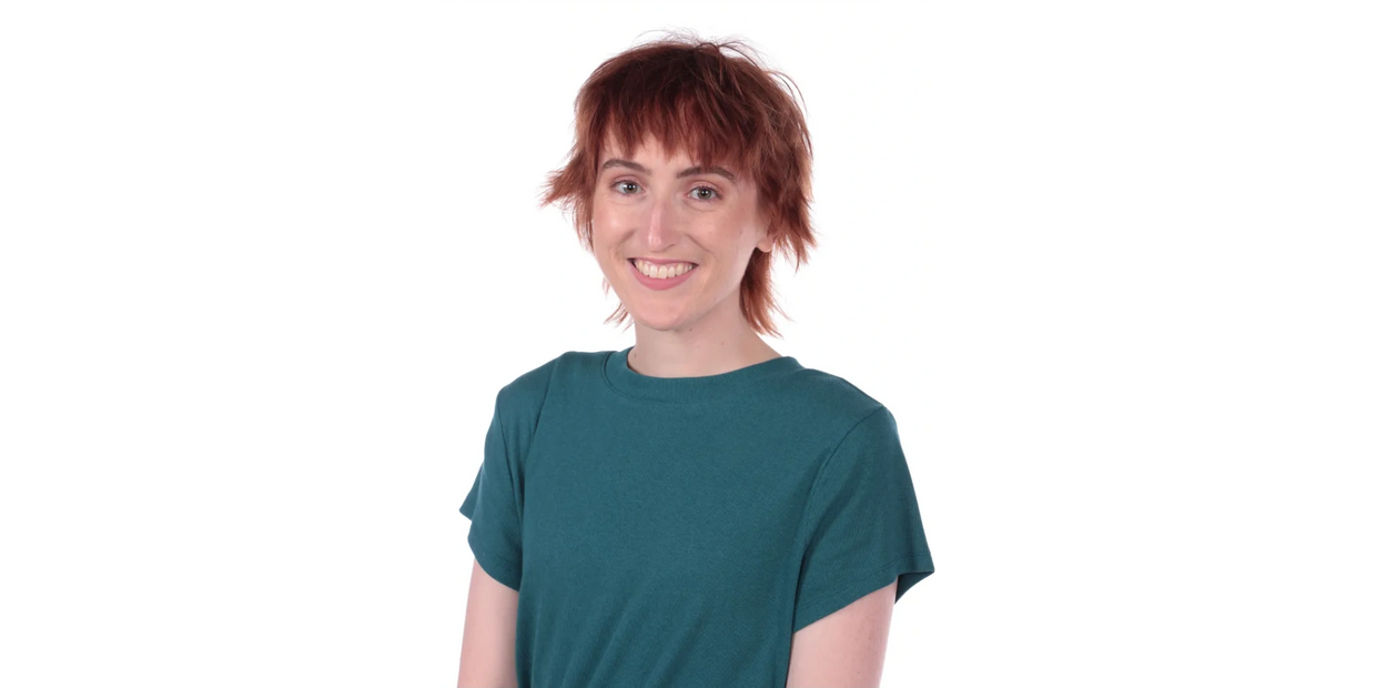 Smiling person with short red hair and teal shirt against white background.