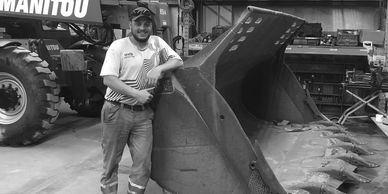 Bandon Blakemore, Co-owner leaning on a large equipment bucket rebuilt in shop