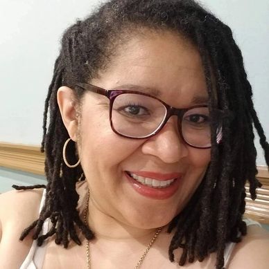 Woman with glasses and dreadlocks smiling warmly.