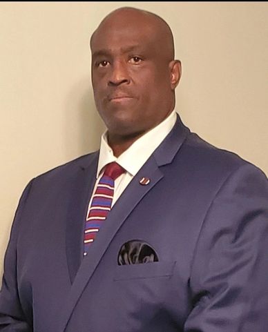 Man in a blue suit with a striped tie posing against a plain background.