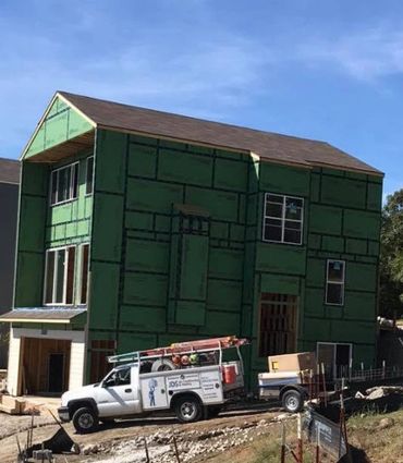 A house under construction with green sheathing and a white work truck parked outside.