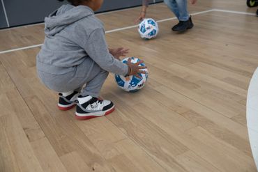Child in gray outfit playing with a blue and white ball indoors.