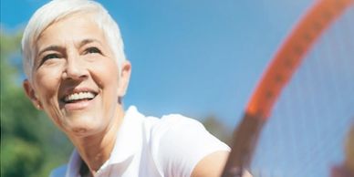 Smiling senior woman playing tennis outdoors on a sunny day.