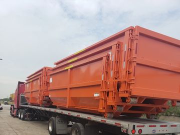 Truck carrying large orange industrial dumpsters.