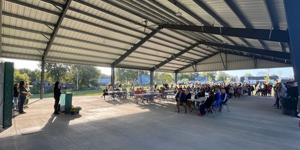 Community event with speakers and seated attendees under a large pavilion.