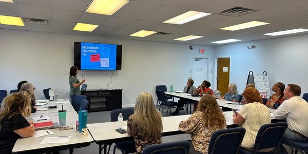 A woman presents storytelling tips to an attentive group in a conference room.