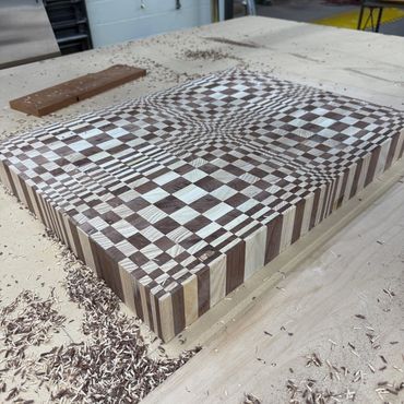Intricately patterned wooden cutting board with wood shavings around it.