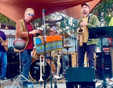 Outdoor band playing diverse instruments under a canopy.