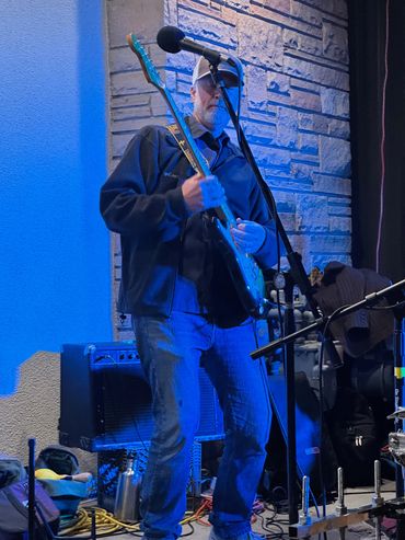 A man playing electric guitar on stage under blue lighting.