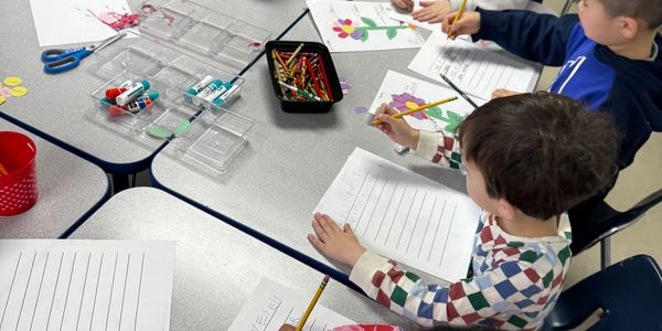 Children coloring and writing at a classroom table.
