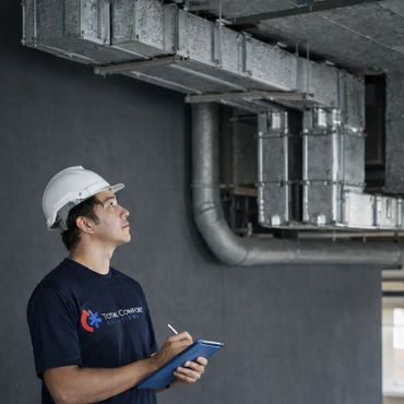 Technician inspecting HVAC ductwork while taking notes on a tablet.