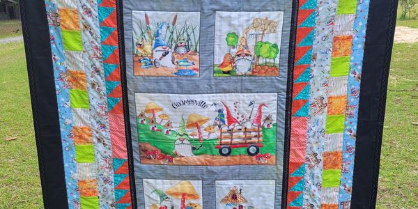 Colorful quilt featuring whimsical gnome and mushroom designs with vibrant patchwork borders.