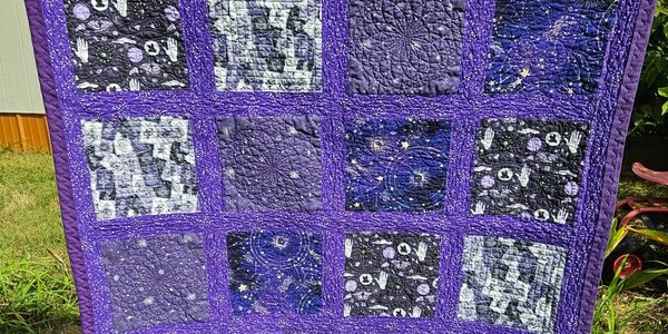 Purple and dark themed quilt with celestial and abstract patterns.