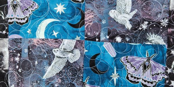 Quilt with purple moths, white owls, and celestial motifs in blue and purple patches.
