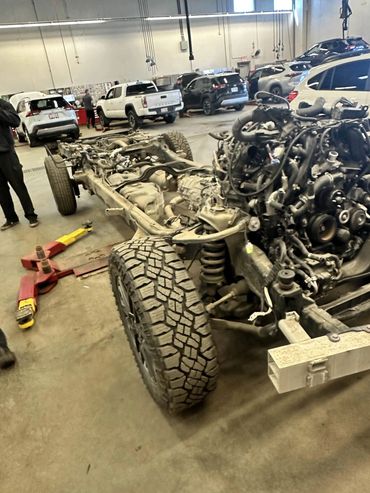 Vehicle chassis with engine and tires in a busy auto repair shop.