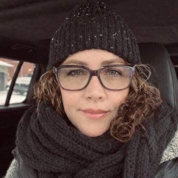 Woman in winter attire with glasses and curly hair.