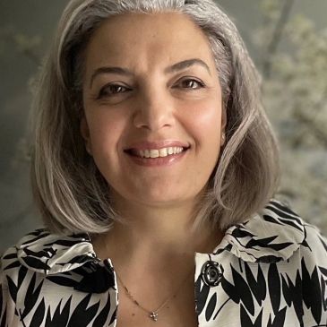 Smiling woman with grey hair and patterned top.