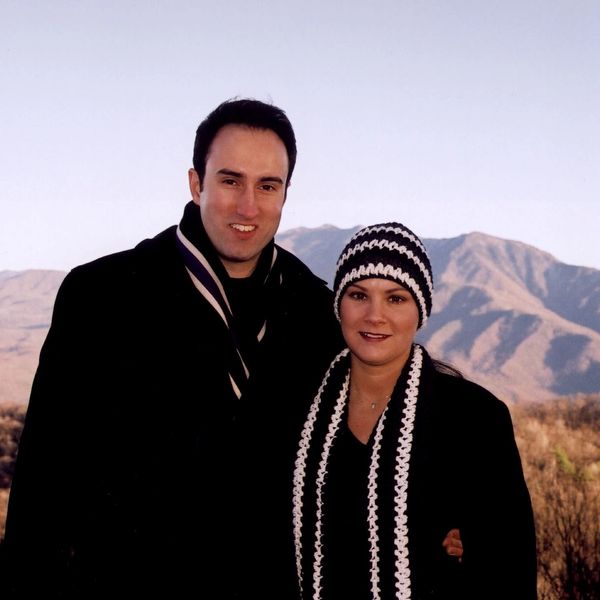 Couple in winter attire posing outdoors with mountains in the background.