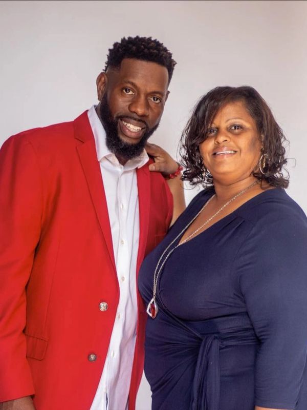 A smiling man in a red jacket and a woman in a navy dress pose together.