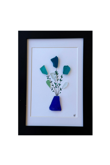 Framed sea glass art depicting a vase with flowers made from colored glass pieces and ink.