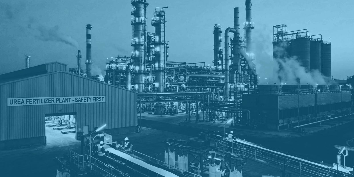 Industrial urea fertilizer plant with workers and large processing towers emitting steam.