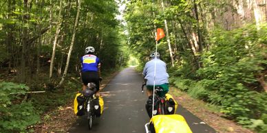 The back of two men on bikes packed with camping gear, riding down a bike path.