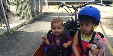 Two kids sitting in the bucket of a cargo bike.