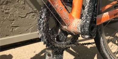 Close-up of an orange bike with a very dirty chain ring, chain and pedals.