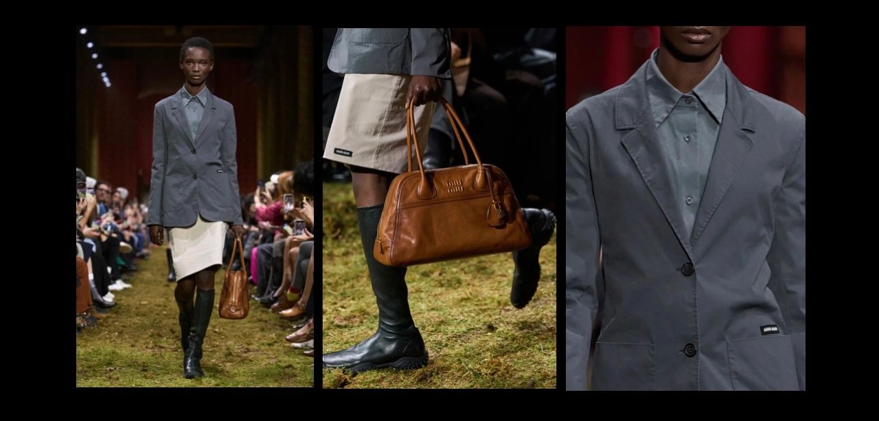 Fashion model in gray blazer, cream skirt, black boots, carrying brown leather bag on runway.