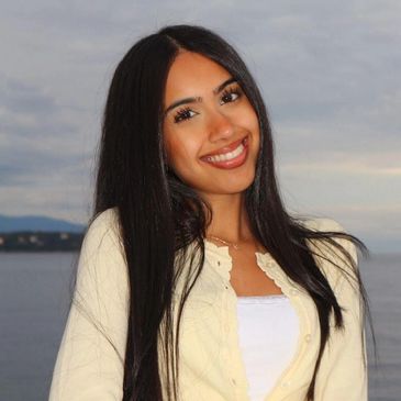 Smiling woman with long black hair in front of a body of water.