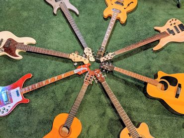 A circle of various guitars and basses arranged on green carpet.