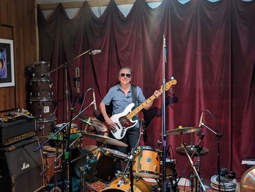 A man with sunglasses playing a bass guitar in a music studio.