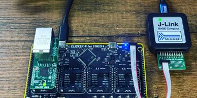 Embedded development board connected to a J-Link debugger on a wooden surface.