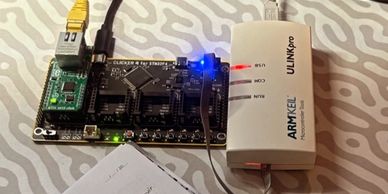 A microcontroller board connected to an ARK-EL ULINKpro debugger with status LEDs on.