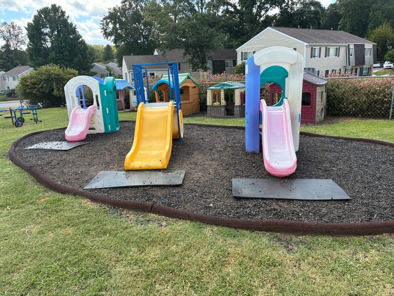 A small playground with colorful slides and playhouses in a residential area.
