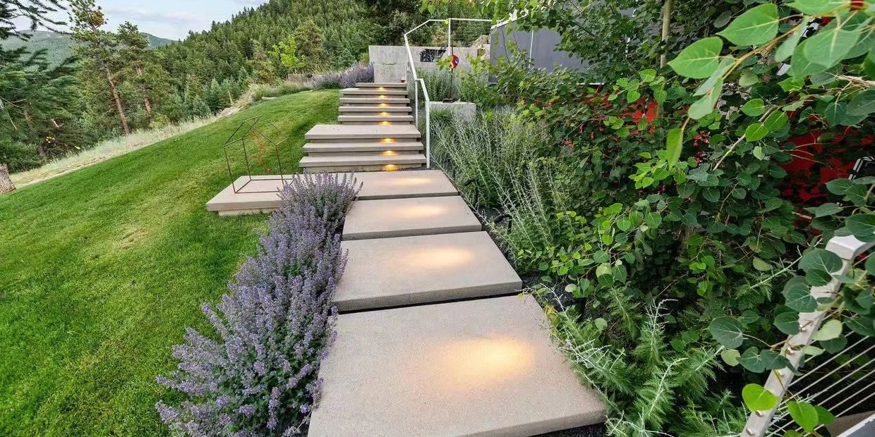 Modern outdoor pathway with illuminated steps and lush greenery on both sides.