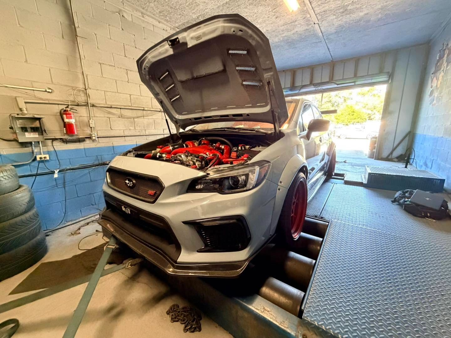 White Subaru STI on a dynamometer with hood open.